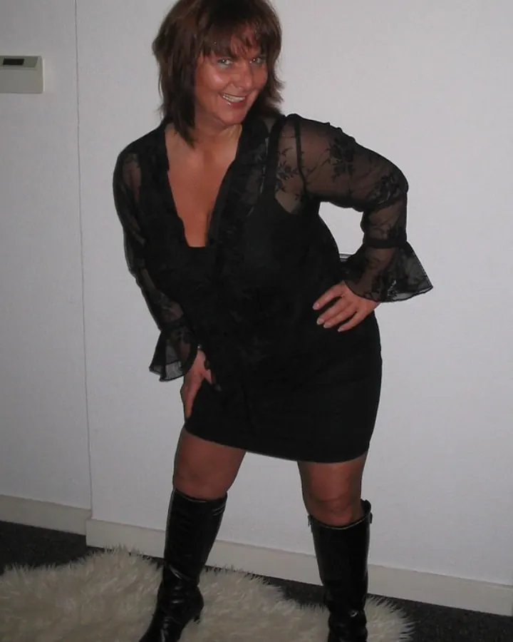Femme en robe noire en dentelle avec bottes hautes, posant sur une fourrure blanche.