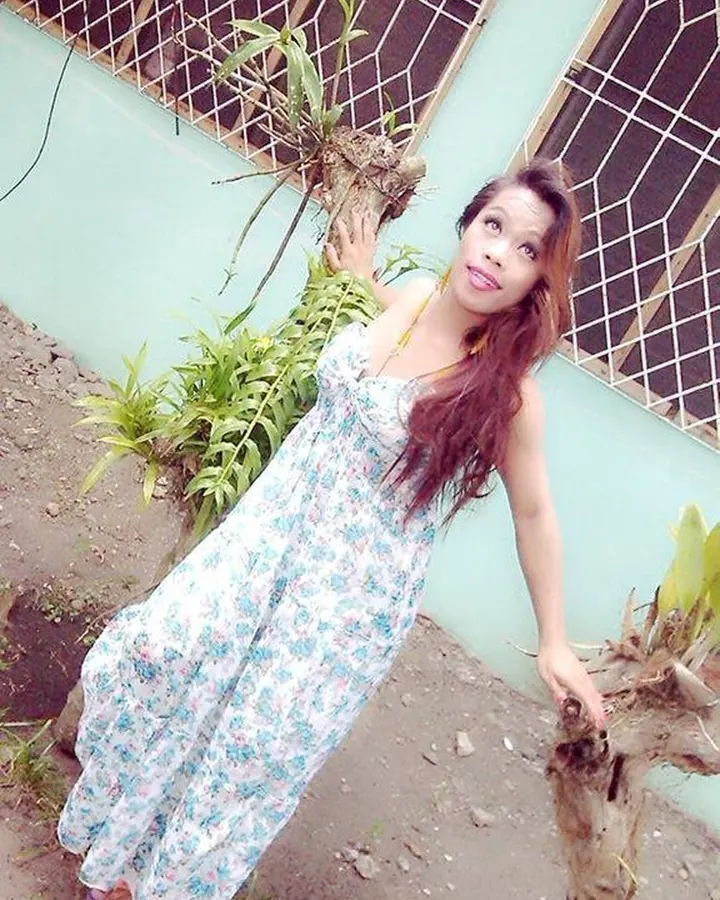 Femme en robe fleurie, tenant une plante, devant un mur turquoise