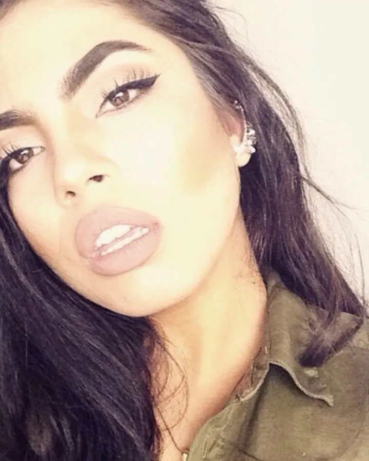 Femme aux cheveux noirs, en chemise verte, faisant un baiser à la caméra, regardant vers le haut.