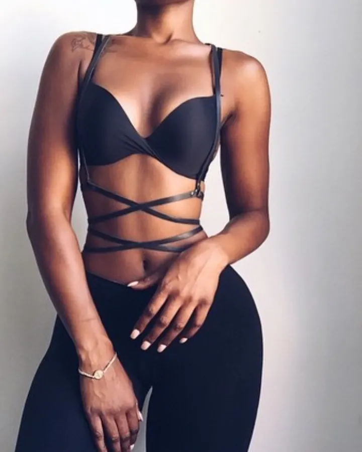 Femme aux cheveux bruns foncés, portant un haut noir transparent avec des bretelles rouges, les mains jointes devant elle, regardant l'appareil.