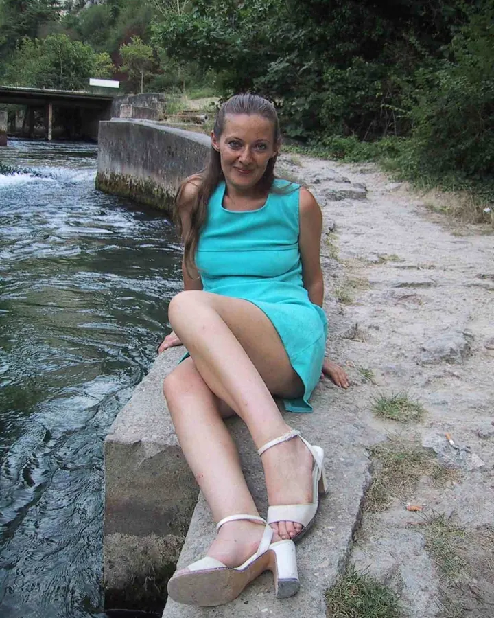 Femme aux cheveux bruns portant un maillot de bain noir, assise sur une plage avec un chapeau bleu