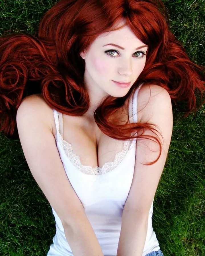 Jeune femme aux cheveux roux allongée sur l'herbe, vêtue d'un haut blanc à dentelle.