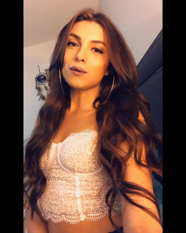 Jeune femme asiatique aux cheveux châtains, regardant l'appareil photo, vêtue d'un haut en dentelle blanche.