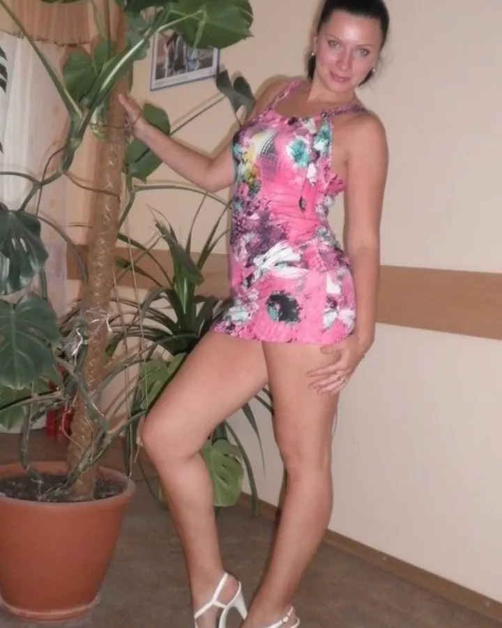 Femme mûre en robe imprimée, mains sur les hanches, regard direct, ambiance intime