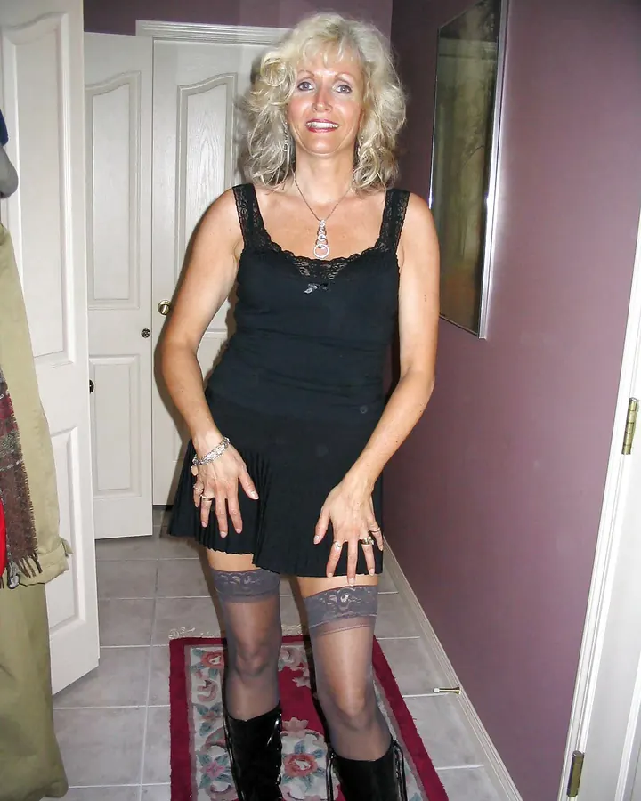 Femme blonde bouclée en robe noire courte et bottes