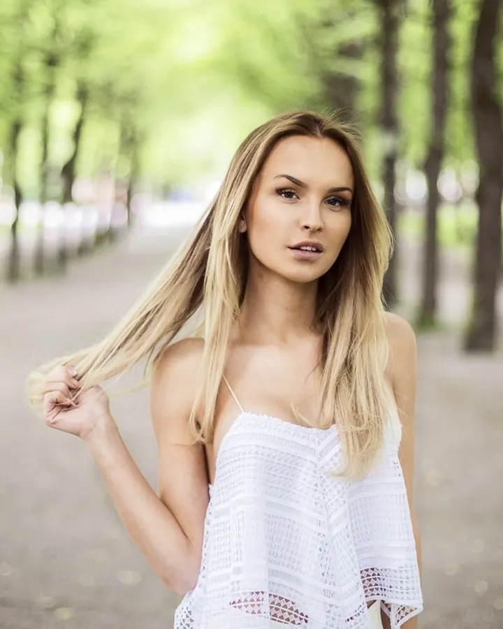 Jeune femme blonde en haut blanc ajouré, marche dans un parc arboré.