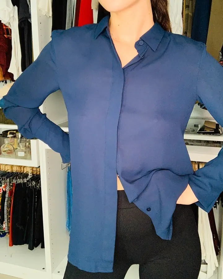 Femme en chemise bleue transparente et leggings noirs, pose devant un dressing ouvert.