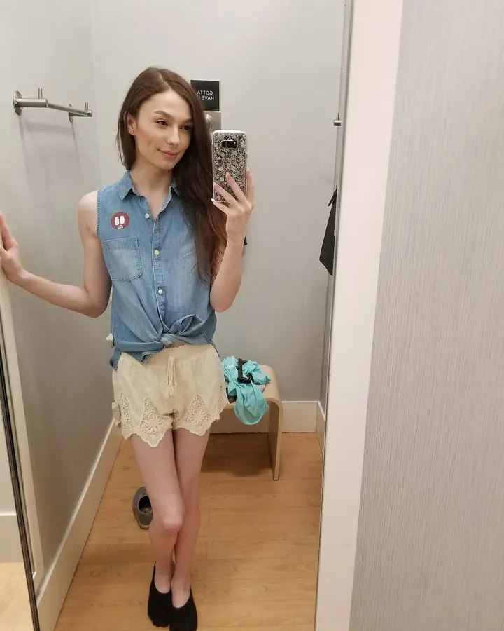 Jeune femme aux cheveux bruns, en tenue décontractée, prenant un selfie dans une cabine d'essayage.