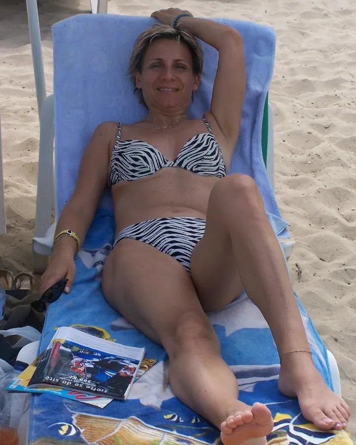 Femme blonde en maillot zèbre, allongée sur une chaise longue sur la plage.