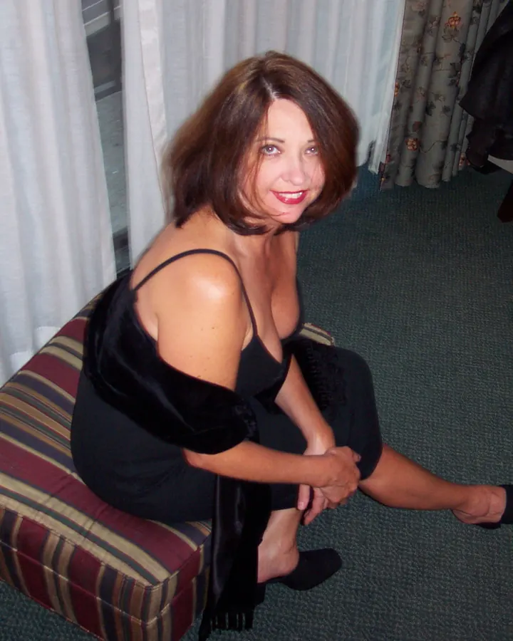 Femme aux cheveux châtains, en tenue simple, posant sur un lit, dans une chambre aux tons clairs.