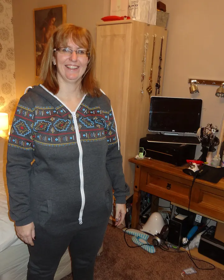 Femme blonde portant une robe noire, posant en intérieur avec un sourire.