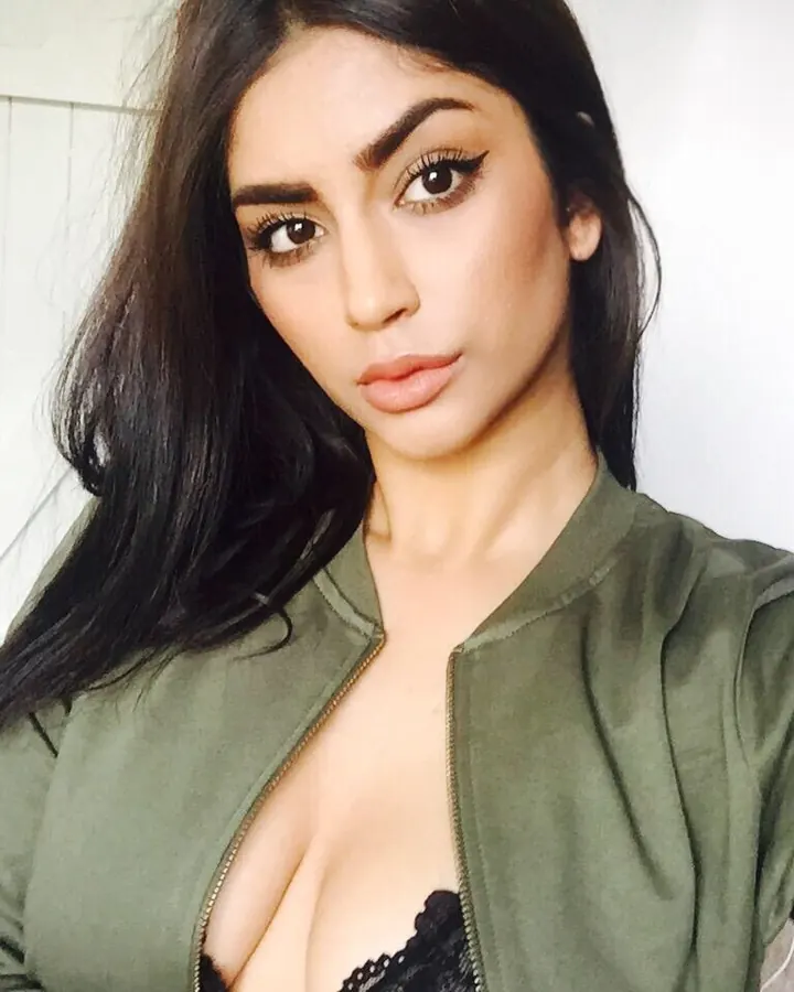 Femme aux cheveux bruns-noirs portant une veste verte, regardant l'appareil photo avec un maquillage soigné.